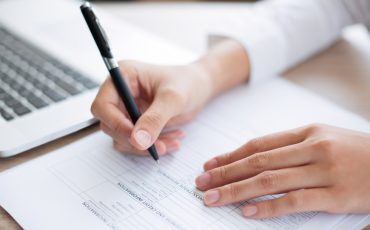 Cropped view of person holding pen and filling out application form on table